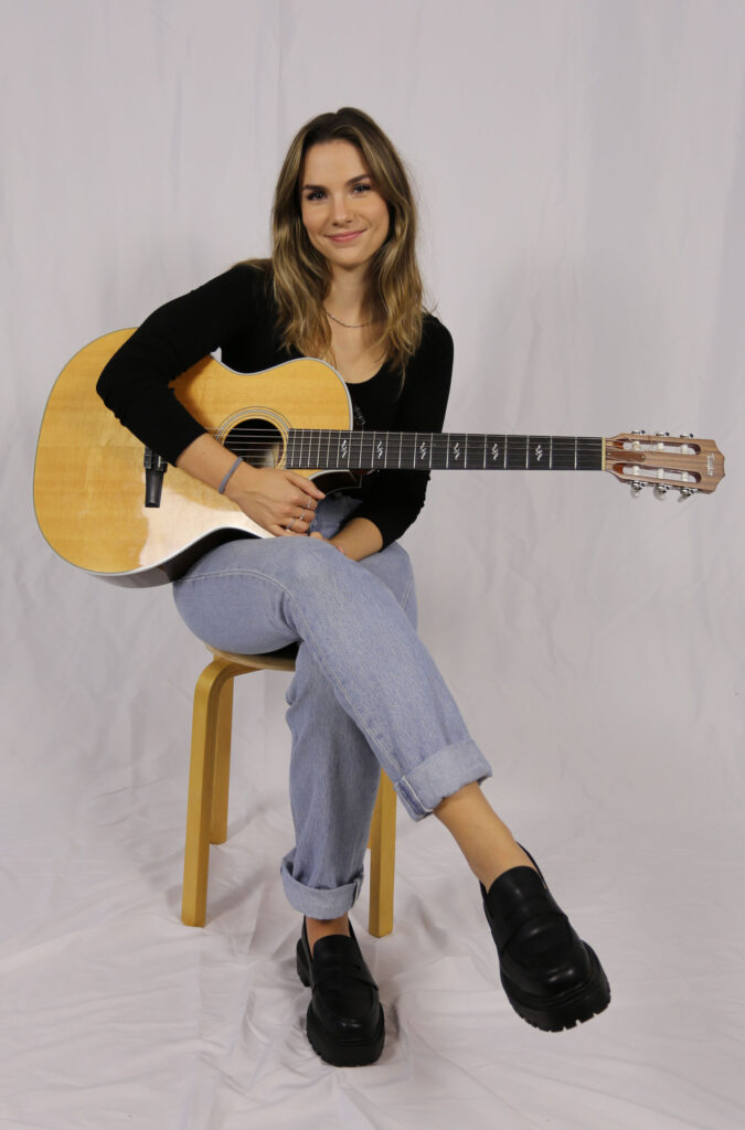 Abbi Berry sitting on stool, holding guitar